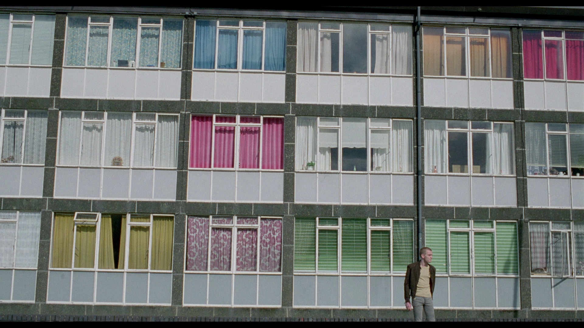 Screenshot from the remastered blu-ray of Trainspotting depicting the title card for Ewan McGregor's character Renton standing in front of an apartment building